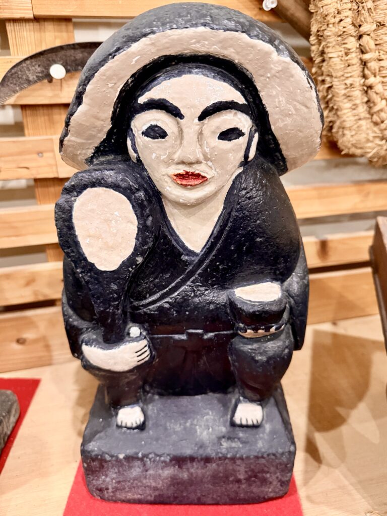 Rice field god with bowl-shaped hat and holding a rice scooper, pained with a black robe and hat, black eyebrows and eyes, and red lips.