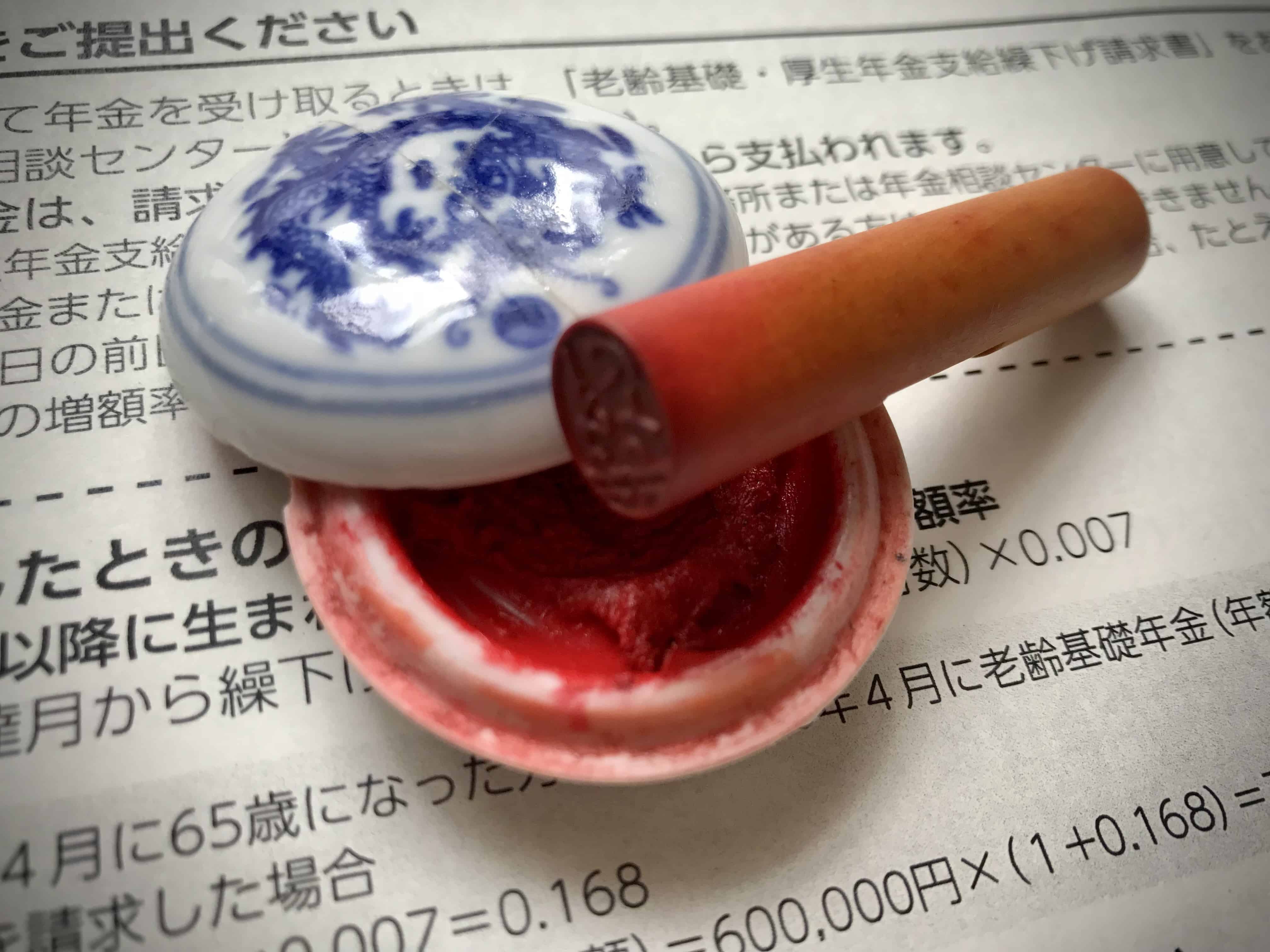 Bamboo carved name stamp resting on a tub of red ink over a background of Japanese text.