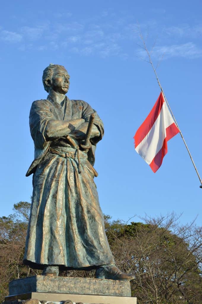 Statue of Sakamoto Ryoma beside the flag of his navy and trading company, Kaentai.