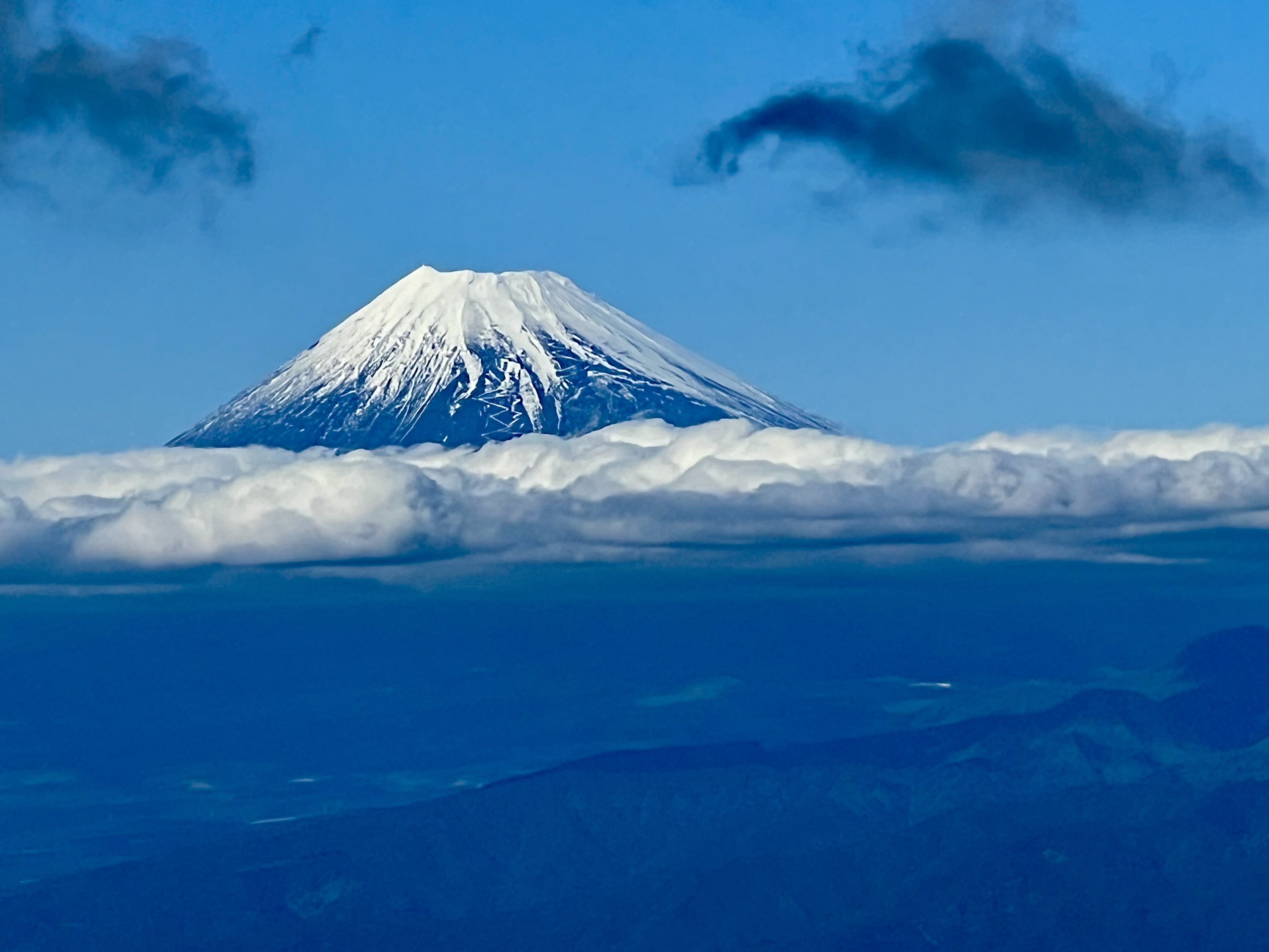 Snow-capped Mount Fuji above clouds and against a blue sky.