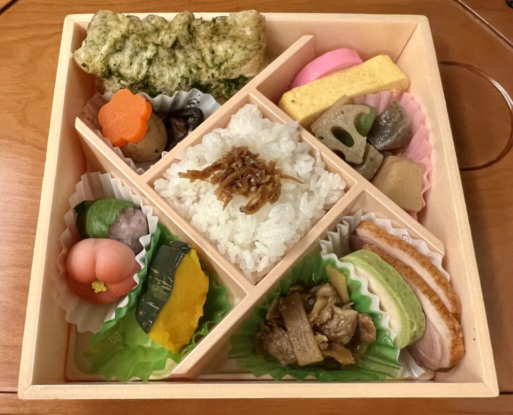 A bento box lunch with vegetables, konnyaku, beef, and rice.