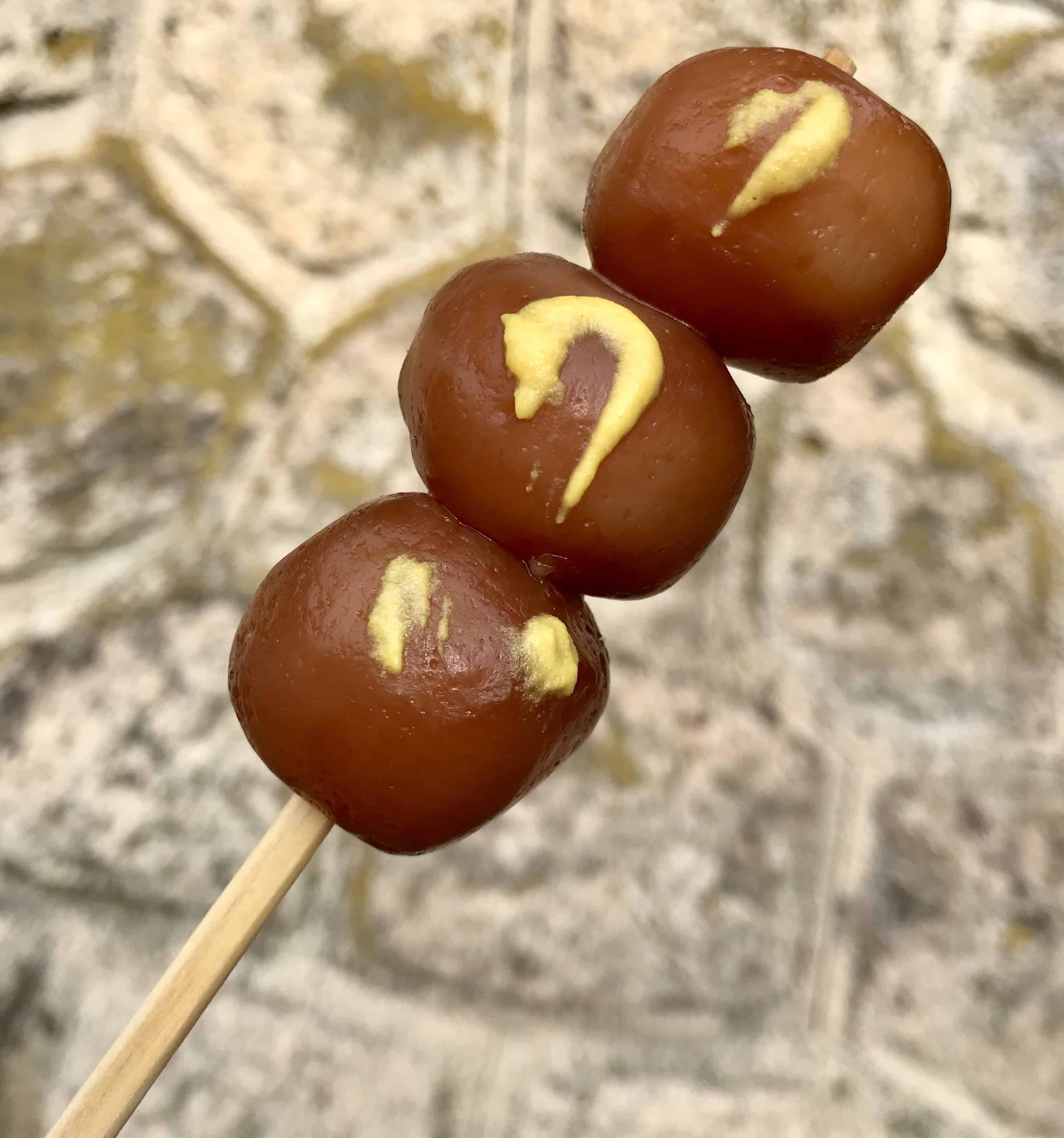 Three balls of brown konnyaku on a skewer, seasoned with karashi hot mustard.