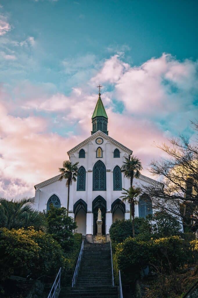 White simple Catholic church against a blue sky with pink clouds.