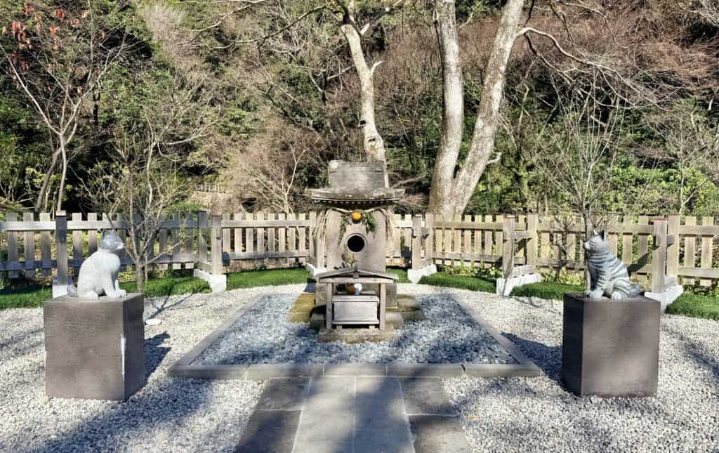 Simple stone shrine flanked by cat statues, set in a forest.